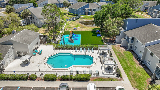 Vibrant apartment complex featuring a sparkling pool, modern lounge area, and a fun playground set amidst lush greenery. - Vista North
