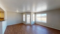 This single-floor unit offers a practical and well-organized layout across its main living areas. The open living room is a standout feature, showcasing rich, dark wood-look flooring that runs throughout the main living spaces. A textured ceiling adds subtle depth, while multiple large windows and a glass-panel door flood the room with natural light and provide outdoor views of the surrounding landscape. The living area also includes direct access to an exterior door, lending a sense of openness to the space.

The kitchen is efficiently designed with ample white cabinetry providing generous storage, dark granite-style countertops, and a full suite of black appliances including a refrigerator, electric range, and an under-cabinet range hood. A double stainless steel sink rounds out the functional workspace, and warm overhead lighting illuminates the area effectively.

The bedroom is finished with plush carpeting, neutral-toned walls, and a full-width sliding closet, offering comfortable and practical personal space. A window brings in natural light, maintaining the bright character found throughout the unit.

The bathroom features wood-look flooring consistent with the main living areas, a single-sink vanity with a granite-style countertop, a full-size soaking tub with a tiled shower surround, and clean, white fixtures throughout. Overall, the unit presents a clean, move-in-ready aesthetic with consistent finishes across all rooms.