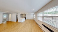 This single-floor unit in East Norwich, NY offers a clean, contemporary design with an open-concept living and kitchen area that creates a generous, airy feel. Light hardwood-style flooring runs throughout the main living space, complementing the bright white walls and recessed lighting overhead. Large windows allow natural light to fill the room, while a baseboard heating system ensures year-round comfort.

The kitchen is well-appointed with grey shaker-style cabinetry, white quartz countertops, a subway tile backsplash, and a full suite of stainless steel appliances, including a refrigerator, dishwasher, microwave, and range. A central island with pendant lighting above serves as both a prep area and a casual gathering point, seamlessly connecting the kitchen to the living space.

A dedicated laundry room provides added convenience, housing a full-size washer and dryer with overhead shelving for storage. The bathroom features a tub-shower combination with white subway tile surround and brushed nickel fixtures, maintaining the unit's cohesive, modern aesthetic. The overall layout, as seen in the 3D model, is thoughtfully organized to maximize functionality and flow throughout the space.