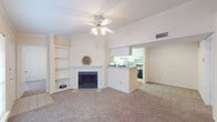This single-floor residence features a neutral, light-filled interior with a well-considered layout connecting living, dining, and kitchen areas. The living room serves as the focal point, showcasing a wood-burning fireplace framed by a clean white mantel and flanked by a built-in shelving unit ideal for display or storage. Crown molding lines the ceiling, and a ceiling fan provides year-round comfort. Soft carpeting extends throughout the living and bedroom areas, contributing to a warm, cohesive aesthetic.

The kitchen is accessible via a pass-through counter that maintains an open connection to the living space. It features a galley-style layout with white cabinetry lining both sides, light wood-tone flooring, and a full suite of appliances including a range, refrigerator, and dishwasher. Ample counter space and cabinet storage make the kitchen functional and efficient.

The bedrooms are generously proportioned, each equipped with ceiling fans and carpeting. One bedroom includes a walk-in closet, while large windows allow natural light to fill the rooms. Two full bathrooms are present, each featuring a tiled tub-shower combination and white cabinetry. An additional carpeted room with crown molding offers flexible use as a dining area or office.