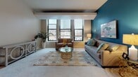 Located at 892 Main St in Hartford, CT, this single-floor residence offers a thoughtfully designed layout with a range of functional and stylish living spaces. The living room is a standout area, featuring large windows that frame urban city views and flood the space with natural light. Architectural beam details accent the ceiling, while a bold teal accent wall adds a striking visual contrast to the neutral tones throughout. The dining area is positioned adjacent to the living room, highlighted by a modern pendant light and carpeted flooring that flows consistently throughout the space. The kitchen is efficiently arranged with light maple cabinetry, stone-toned countertops, and stainless steel appliances including a range and over-the-range microwave. The primary bedroom is generously proportioned, offering large windows with city views, soft carpeting, and direct access to a spacious walk-in closet fitted with dual clothing rails and shelving. A second bedroom provides a comfortable retreat with its own window and closet access. The bathroom features tile flooring, a light wood vanity with stone countertops, and a clean, functional design. Completing the unit is a dedicated in-unit laundry room equipped with a full-size washer and dryer alongside wire shelving for additional storage.