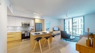 Located at 5700 Biscayne Blvd in Miami's vibrant MiMo district, this contemporary residence offers a seamlessly open-concept design bathed in natural light. Light-toned hardwood flooring flows throughout, unifying the living, dining, and kitchen areas into a cohesive, airy environment.

The kitchen is a standout feature, showcasing a combination of white upper cabinetry and warm wood lower cabinets, a textured tile backsplash, stainless steel appliances, and a generous island with bar seating — ideal for casual dining and entertaining. The open living area extends naturally toward floor-to-ceiling sliding glass doors that open to a private balcony, providing views of the surrounding modern architecture and allowing ample sunlight to fill the space.

Both bedrooms are well-proportioned and bright, each featuring large floor-to-ceiling windows, ceiling fans, and herringbone-patterned flooring, creating a calm and refined retreat. The bathroom is finished with a floating wood vanity, a white quartz countertop, and a backlit mirror, lending a clean, spa-like aesthetic.

The entryway is practical and welcoming, with louvered closet doors and light wood finishes that set the tone for the modern, warm interior design found throughout this thoughtfully appointed Miami residence.