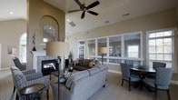 This single-story clubhouse is designed to offer residents a comfortable and functional gathering space. The main lounge area is defined by dramatically vaulted ceilings and a ceiling fan that enhances airflow and comfort throughout. A classic fireplace serves as a focal point, framed by an elegant arched architectural niche that adds a refined decorative touch to the warm, neutral-toned walls.

The lounge is furnished with plush seating arrangements, including a gray sectional sofa and accent chairs, creating an inviting atmosphere for relaxation or socializing. A dedicated seating area with a dark table and chairs provides space for casual dining or activities. Large interior windows along one wall offer a clear view into an adjoining fitness room equipped with exercise equipment, seamlessly connecting the social and wellness amenities of the clubhouse.

Natural light filters in through the windows, brightening the space and contributing to its open, airy feel. The interior design strikes a balance between casual comfort and polished style, with coordinated furnishings, soft textiles, and tasteful décor accents throughout. Overall, this clubhouse delivers a well-appointed community retreat that caters to both leisure and active lifestyles.