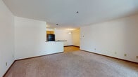 This single-floor unit offers a practical and well-organized layout designed for comfortable everyday living. The open-concept living area is finished with neutral wall-to-wall carpeting and clean white walls, creating a bright and versatile space. A half-wall peninsula visually separates the living area from the kitchen while maintaining an open flow between the two spaces. Large sliding glass doors in the living area invite natural light and provide outdoor views of surrounding greenery, enhancing the overall sense of openness.

The galley-style kitchen is efficiently designed, featuring warm honey-toned wood cabinetry, dark countertops, and durable wood-look plank flooring. Black appliances — including a refrigerator, range, and dishwasher — provide a cohesive look, while ample cabinetry offers generous storage. A double basin sink adds to the kitchen's functionality.

The bedroom is a comfortable, carpeted retreat equipped with a ceiling fan and a window overlooking the outdoors. An adjacent walk-in closet provides substantial storage space with built-in shelving and hanging rods.

The bathroom features tile flooring, a wide single-sink vanity with dark countertops and wood cabinetry, a large mirror, and chrome hardware accents, lending a clean and functional aesthetic throughout.