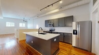 Located at 123 E Dunbar St in Spartanburg, SC, this two-story home offers a well-designed layout across two floors. The main level hosts an open-plan kitchen and living area bathed in natural light from multiple windows. The kitchen is a standout feature, equipped with stainless steel appliances including a range, microwave, and refrigerator, complemented by gray shaker-style cabinetry, white quartz countertops, and a large central island with a black undermount sink — all set atop rich, warm hardwood floors. Track lighting and exposed ductwork lend an industrial-modern character to the space. The upper level houses the generously proportioned primary bedroom, featuring vaulted ceilings, gleaming hardwood floors, multiple windows for abundant natural light, and a ceiling fan. An attached walk-in closet provides ample storage with wrap-around shelving. The two bathrooms are finished with gray vanities, white quartz countertops, and neutral tile flooring, with one featuring a round mirror and a window for natural light. The lower level offers a versatile bonus area with carpeted floors, an exposed beam ceiling, and built-in shelving — ideal for a home office, media room, or recreation space. A utility room completes the layout, adding practical functionality to this thoughtfully appointed home.