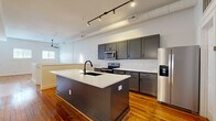 Located at 123 E Dunbar St in Spartanburg, SC, this two-story home offers a well-designed layout across two floors. The main level hosts an open-plan kitchen and living area bathed in natural light from multiple windows. The kitchen is a standout feature, equipped with stainless steel appliances including a range, microwave, and refrigerator, complemented by gray shaker-style cabinetry, white quartz countertops, and a large central island with a black undermount sink — all set atop rich, warm hardwood floors. Track lighting and exposed ductwork lend an industrial-modern character to the space. The upper level houses the generously proportioned primary bedroom, featuring vaulted ceilings, gleaming hardwood floors, multiple windows for abundant natural light, and a ceiling fan. An attached walk-in closet provides ample storage with wrap-around shelving. The two bathrooms are finished with gray vanities, white quartz countertops, and neutral tile flooring, with one featuring a round mirror and a window for natural light. The lower level offers a versatile bonus area with carpeted floors, an exposed beam ceiling, and built-in shelving — ideal for a home office, media room, or recreation space. A utility room completes the layout, adding practical functionality to this thoughtfully appointed home.