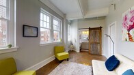 Located at 43 W Long St in the heart of downtown Columbus, Ohio, this urban loft-style unit blends industrial character with modern comfort. The open layout is anchored by polished concrete floors that run throughout, reflecting natural light and lending a sleek, contemporary feel to the space.

The main living area is bright and airy, lined with an impressive row of large double-hung windows that frame views of the surrounding historic brick architecture of the Columbus cityscape. The generous window presence floods the space with natural light and creates an inviting, open atmosphere.

A standout architectural detail is the reclaimed wood sliding barn door, which provides a stylish transition into the bathroom. The bathroom is well-appointed with a clean white vanity featuring a vessel-style sink, stone countertop, and a window that continues the theme of natural light throughout.

The kitchen is efficiently designed with gray shaker-style cabinetry extending to the ceiling, stainless steel appliances including a refrigerator, range, built-in microwave, and dishwasher, along with light countertops and a utility sink. A butcher block prep table adds warmth and additional workspace.

Elevated ceilings with exposed structural elements reinforce the loft aesthetic, while the neutral gray wall palette and polished floors create a versatile backdrop suited to a variety of uses.