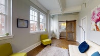 Located at 43 W Long St in the heart of downtown Columbus, Ohio, this urban loft-style unit blends industrial character with modern comfort. The open layout is anchored by polished concrete floors that run throughout, reflecting natural light and lending a sleek, contemporary feel to the space.

The main living area is bright and airy, lined with an impressive row of large double-hung windows that frame views of the surrounding historic brick architecture of the Columbus cityscape. The generous window presence floods the space with natural light and creates an inviting, open atmosphere.

A standout architectural detail is the reclaimed wood sliding barn door, which provides a stylish transition into the bathroom. The bathroom is well-appointed with a clean white vanity featuring a vessel-style sink, stone countertop, and a window that continues the theme of natural light throughout.

The kitchen is efficiently designed with gray shaker-style cabinetry extending to the ceiling, stainless steel appliances including a refrigerator, range, built-in microwave, and dishwasher, along with light countertops and a utility sink. A butcher block prep table adds warmth and additional workspace.

Elevated ceilings with exposed structural elements reinforce the loft aesthetic, while the neutral gray wall palette and polished floors create a versatile backdrop suited to a variety of uses.