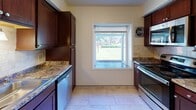 This single-floor residence offers a thoughtfully designed layout that balances functionality with comfort. The kitchen is a standout feature, equipped with rich dark-wood cabinetry, granite countertops, a travertine tile backsplash, stainless steel appliances — including a range, microwave, and dishwasher — and light tile flooring. A centered window frames a pleasant view of the surrounding greenery, filling the space with natural light.

The living area is generously sized, featuring neutral wall tones, plush wall-to-wall carpeting, and a large window that further connects the interior to the outdoors. A pendant light fixture near the entry adds a welcoming touch. The front entry transitions seamlessly from tile to carpet, creating a clean division between spaces.

Multiple carpeted bedrooms offer comfortable, quiet retreats, each with windows that allow natural light to brighten the rooms. The neutral color palette throughout provides a versatile backdrop for a variety of furnishing styles.

The bathroom is well-appointed, featuring large-format tile flooring, a tiled soaking tub and shower combination with decorative mosaic accent borders, a dark-wood vanity with an integrated sink, a framed mirror, and a window that provides ventilation and natural light. Overall, the space presents a clean, move-in-ready environment with consistent finishes throughout.