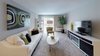 This single-story residence offers a practical and well-organized layout across several distinct areas. The living room serves as the central gathering space, finished with plush wall-to-wall carpeting and neutral-toned walls that create a calm, inviting atmosphere. A sliding glass door floods the room with natural light and provides direct access to an outdoor patio, enhancing the sense of openness. The space accommodates a generous seating arrangement alongside a media console, making it well-suited for both relaxing and entertaining.

The kitchen is efficiently designed with dark wood cabinetry providing ample storage above and below the countertops. White appliances, including a range and oven, complement the light countertop surfaces, while a double-basin stainless steel sink adds functionality. The patterned tile flooring ties the space together with a classic look.

The bedroom, visible in the floor plan, is a private retreat positioned away from the main living areas. The full bathroom features mosaic tile flooring, a tub-shower combination, a single vanity with cabinet storage, and built-in shelving near the entrance for added convenience. Overall, the residence presents a clean, functional design with a cohesive neutral color palette throughout.