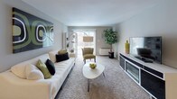 This single-story residence offers a practical and well-organized layout across several distinct areas. The living room serves as the central gathering space, finished with plush wall-to-wall carpeting and neutral-toned walls that create a calm, inviting atmosphere. A sliding glass door floods the room with natural light and provides direct access to an outdoor patio, enhancing the sense of openness. The space accommodates a generous seating arrangement alongside a media console, making it well-suited for both relaxing and entertaining.

The kitchen is efficiently designed with dark wood cabinetry providing ample storage above and below the countertops. White appliances, including a range and oven, complement the light countertop surfaces, while a double-basin stainless steel sink adds functionality. The patterned tile flooring ties the space together with a classic look.

The bedroom, visible in the floor plan, is a private retreat positioned away from the main living areas. The full bathroom features mosaic tile flooring, a tub-shower combination, a single vanity with cabinet storage, and built-in shelving near the entrance for added convenience. Overall, the residence presents a clean, functional design with a cohesive neutral color palette throughout.