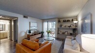 This single-floor residence is thoughtfully laid out to maximize comfort and functionality throughout. The living room serves as the heart of the home, featuring wood-look flooring, a textured ceiling, and built-in shelving that provides both storage and display space. A sliding glass door floods the room with natural light and opens to a private outdoor balcony, creating a seamless indoor-outdoor connection. The adjacent dining area is an intimate nook accented by decorative wall art and a round wood dining table, offering a cozy setting for meals. The kitchen is well-equipped with granite-style countertops, gray cabinetry, a tile backsplash, and black appliances including an electric range with an overhead stainless steel microwave. A separate laundry area is conveniently accessible from the kitchen. The bedroom is a tranquil retreat with wood-look flooring, a ceiling fan, and a window that allows soft natural light to filter in. The full bathroom features a wide vanity with granite-style countertops, ample cabinetry, a large mirror with overhead lighting, and a tub-shower combination. Consistent wood-look flooring and a neutral color palette tie the entire space together in a cohesive, modern aesthetic.