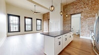 This 930 square foot, single-floor apartment in Hamilton, Ohio offers a harmonious blend of modern comfort and industrial chic. The space boasts a generous one-bedroom layout with an expansive 230 square foot primary bedroom. The open-concept design seamlessly integrates the kitchen and living areas, creating a fluid, spacious feel.

The apartment's standout feature is its stunning exposed brick wall, adding character and warmth to the contemporary setting. Large windows with striking navy blue frames flood the rooms with natural light and provide picturesque views of the surrounding area.

The kitchen is a chef's dream, featuring sleek white cabinetry, stainless steel appliances, and a substantial island with a dark granite countertop. Modern pendant lighting enhances the aesthetic appeal while providing functional illumination.

The bathroom continues the apartment's stylish theme with a clean, white palette, wood-look flooring, and a granite vanity top. A notable grey sliding door adds a touch of sophistication.

Throughout the apartment, warm wood-toned flooring creates a cohesive look and enhances the overall sense of space. The blend of industrial elements with modern finishes results in a unique, inviting living space that's both comfortable and visually appealing.