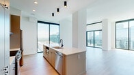 Located in Atlanta's vibrant Midtown neighborhood, this contemporary 3-bedroom, 4-bathroom residence offers a sleek, modern design throughout. Light-toned hardwood flooring flows seamlessly across the entire single-floor layout, complementing the clean white walls and minimalist aesthetic.

The open-concept kitchen and living area serves as the heart of the home, featuring a large center island with a white quartz countertop, a matte black faucet, and stainless steel appliances including a dishwasher and refrigerator. Warm taupe cabinetry lines the kitchen walls, while track pendant lighting adds a modern touch. Floor-to-ceiling windows and sliding glass doors flood the living area with natural light and frame sweeping panoramic views of the Atlanta skyline and surrounding cityscape, with access to a private balcony.

Each of the three bedrooms is generously proportioned, with the primary suite offering a dedicated walk-in closet outfitted with custom shelving and drawers. The primary bathroom features marble-tiled flooring, a white quartz vanity, matte black fixtures, and a glass-enclosed shower with subway tile surround. Additional bathrooms maintain the same refined aesthetic with clean vanities and contemporary hardware.

Clean hallways with recessed lighting and gray-accented doors complete this thoughtfully designed urban residence.