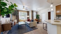 This thoughtfully designed single-floor residence offers a welcoming and functional layout that balances comfort with everyday practicality. The open-concept living area serves as the heart of the home, featuring plush carpet flooring, a ceiling fan, and multiple windows dressed with elegant drape panels and blinds that bathe the space in natural light. A glass-top coffee table and generous sofa provide a relaxed setting, while a defined dining nook with bar-height seating sits adjacent, creating a seamless flow for entertaining.

The kitchen is well-equipped with warm wood cabinetry, stainless steel appliances including a range, microwave, and refrigerator, and a mosaic tile backsplash that adds a decorative accent. Light stone countertops and a peninsula with seating enhance both functionality and style. Light wood-tone flooring carries throughout the kitchen for easy maintenance.

The bedroom is a tranquil retreat, featuring soft carpet, a ceiling fan, and a sliding glass door that opens to a private outdoor patio. A spacious walk-in closet with dual hanging rods and built-in shelving provides ample storage.

The bathroom features light wood-look tile flooring and a clean, neutral palette. Completing the home is a dedicated in-unit laundry area, adding a layer of everyday convenience.