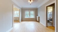 Located at 125 Oak Grove St in Minneapolis's Loring Park neighborhood, this single-floor unit showcases classic architectural details throughout. Warm hardwood floors extend across the living and sleeping areas, complemented by crisp white crown molding and neutral gray walls that create a clean, timeless aesthetic.

The living area is generously proportioned, featuring a ceiling fan, large windows that invite natural light and offer views of surrounding greenery, and a traditional cast-iron radiator. A built-in bookshelf with multiple shelves provides convenient storage and display space, while dark wood doors add character and contrast against the light interior palette.

The galley-style kitchen is accessed through a distinctive arched entryway and is well-appointed with rich dark wood cabinetry, granite-look countertops, and black appliances including a gas range and refrigerator. Open shelving and glass-front cabinet details add a functional, classic charm to the space.

The bathroom retains its vintage character with classic white hex tile flooring, a pedestal sink, a full-sized soaking tub with shower, and a mirrored medicine cabinet. Dark, aged wood door hardware echoes the period-appropriate details found throughout the unit.

Additional highlights include a closet off the main hallway and an entry area with ample door access, making this a well-organized and characterful space in a prime Minneapolis location.