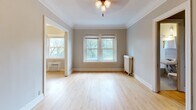 Located at 125 Oak Grove St in Minneapolis's Loring Park neighborhood, this single-floor unit showcases classic architectural details throughout. Warm hardwood floors extend across the living and sleeping areas, complemented by crisp white crown molding and neutral gray walls that create a clean, timeless aesthetic.

The living area is generously proportioned, featuring a ceiling fan, large windows that invite natural light and offer views of surrounding greenery, and a traditional cast-iron radiator. A built-in bookshelf with multiple shelves provides convenient storage and display space, while dark wood doors add character and contrast against the light interior palette.

The galley-style kitchen is accessed through a distinctive arched entryway and is well-appointed with rich dark wood cabinetry, granite-look countertops, and black appliances including a gas range and refrigerator. Open shelving and glass-front cabinet details add a functional, classic charm to the space.

The bathroom retains its vintage character with classic white hex tile flooring, a pedestal sink, a full-sized soaking tub with shower, and a mirrored medicine cabinet. Dark, aged wood door hardware echoes the period-appropriate details found throughout the unit.

Additional highlights include a closet off the main hallway and an entry area with ample door access, making this a well-organized and characterful space in a prime Minneapolis location.
