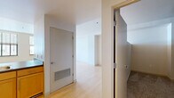 Located in the heart of Kansas City, MO, this single-floor residence offers a clean, modern aesthetic throughout. Light hardwood flooring runs seamlessly across the open-concept kitchen and living area, creating a bright, cohesive feel. The kitchen is thoughtfully equipped with warm maple cabinetry, dark countertops, stainless steel appliances including a refrigerator, range, and dishwasher, and a double sink positioned beneath a window that draws in natural light. The open layout connects the kitchen directly to the living area, which features structural columns that add architectural character while defining the space. Track lighting accents the living area, and windows framing city views contribute to an airy urban atmosphere. The bathroom is finished with tile flooring, a full tub-shower combination, a single vanity with maple cabinetry, and a large mirror. A dedicated walk-in closet provides generous storage, outfitted with wire shelving and hanging rods along two walls over plush carpet flooring. Clean white walls and a neutral palette throughout give the space a versatile, move-in-ready quality suited to a variety of styles.