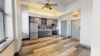 This thoughtfully designed 1-bedroom, 1-bathroom unit makes excellent use of its compact footprint across a single floor. Wide-plank wood-look flooring flows seamlessly throughout the entire space, lending a warm, cohesive aesthetic.

The open-concept kitchen is a standout feature, showcasing dark-toned cabinetry with a built-in wine rack, a mosaic tile backsplash, light countertops, and a full suite of stainless steel appliances including a refrigerator, dishwasher, microwave, and range. A tray ceiling with a brass-accented ceiling fan overhead adds architectural interest and a sense of height to the living area, which is bathed in natural light through multiple windows offering city views.

The bedroom is a quiet, functional retreat with wood-look tile flooring, a large window with city-facing views, and clean, neutral walls that provide a versatile canvas.

The bathroom is finished to a high standard, featuring a dark-framed vanity mirror flanked by sleek vertical light fixtures, a stained wood vanity cabinet with a white countertop, matte black hardware, and a tub-shower combination clad in classic white subway tile. Wood-look tile flooring continues here, tying the space together cohesively. Every detail reflects a modern, urban design sensibility.