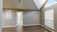 This efficient one-bedroom, two-bathroom single-floor unit offers a thoughtfully organized layout that maximizes every square foot. The combined living, dining, and kitchen area serves as the heart of the home, featuring durable wood-look plank flooring, neutral gray walls, and recessed lighting that creates a clean, modern aesthetic. Built-in open shelving along one wall provides practical storage and display space, while the kitchen is visible beyond, outfitted with warm cabinetry.

A standout architectural feature is the vaulted ceiling with a large arched skylight window in the living area, which draws in abundant natural light and adds a striking sense of vertical space. Two additional windows with blinds further brighten the room.

The bedroom is carpeted for comfort and benefits from its own vaulted ceiling detail, along with windows that allow natural light to filter in. A dedicated closet with mirrored sliding doors adds functional storage. The hallway connecting the rooms is finished with light wood-look flooring and leads to both bathrooms. One bathroom features a full tub-shower combination with clean white surrounds and wood-look flooring. The neutral color palette and white trim throughout the unit provide a cohesive, move-in ready appearance.