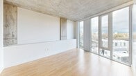 Located at 22 NE 2nd Ave in Portland, Oregon, this modern urban studio offers a well-designed single-floor layout that makes efficient use of its compact footprint. The open living area is a standout, featuring dramatic floor-to-ceiling windows that flood the space with natural light and frame sweeping views of the Portland skyline. Exposed concrete ceilings add an industrial character that complements the clean, contemporary aesthetic throughout.

The kitchen is sleekly appointed with high-gloss gray cabinetry, stainless steel appliances including a range and built-in microwave, a decorative herringbone tile backsplash, and under-cabinet lighting — all set against warm light wood flooring that runs throughout the unit. The living area provides an open canvas, benefiting from both the city views and the raw architectural ceiling detail.

The bedroom area features a large sliding-door closet, offering practical storage within a minimalist design. The bathroom is clean and functional, finished in white with a full soaking tub and shower combination, and modern chrome fixtures. A dedicated laundry nook houses a stacked washer and dryer unit, adding everyday convenience. This residence offers a refined urban living experience in the heart of Portland.