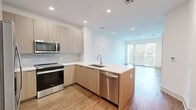 Located at 99 Wilkens Ln in Barnstable, MA, this thoughtfully designed one-bedroom, one-bathroom residence offers a modern aesthetic with high-quality finishes throughout its efficiently utilized single-floor layout. The open-concept kitchen and living area serves as the heart of the home, anchored by a sleek peninsula with a crisp white quartz countertop and undermount sink. The kitchen features light wood flat-front cabinetry, a subway tile backsplash, and a full suite of stainless steel appliances including a French door refrigerator, electric range, built-in microwave, and dishwasher. Wide-plank hardwood flooring flows seamlessly throughout the main living areas, complementing the clean, neutral palette. The living room is bathed in natural light through floor-to-ceiling sliding glass doors that frame lush green outdoor views. The bedroom is a serene retreat with large windows, a ceiling fan, and continued hardwood flooring. The bathroom offers a refined finish with marble-style tile flooring, a floating wood vanity with white countertop, wall-mounted cabinetry, and a clean, minimalist design. A dedicated closet provides additional storage, completing this well-appointed residence.