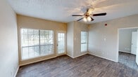 This single-floor unit offers a well-organized layout designed for comfortable everyday living. The main living area serves as the focal point of the space, featuring dark hardwood-style flooring that extends throughout the unit, warm neutral-toned walls, and a textured ceiling. A ceiling fan with integrated lighting is centrally positioned overhead, providing both air circulation and ambient light. Multiple windows fitted with horizontal blinds allow natural light to fill the room, while a glass-paneled door provides direct outdoor access and additional views of the surrounding greenery.

A separate bedroom includes its own window with blinds, continuing the hardwood-style flooring and neutral color palette found throughout the unit. The kitchen is thoughtfully appointed with white cabinetry, granite-style countertops, a white subway tile backsplash, and stainless steel appliances including a refrigerator and electric range. The bathroom features a tub-shower combination and a vanity with a granite-style countertop. Conveniently adjacent to the bathroom, a dedicated closet space houses a stacked washer and dryer unit, adding practical in-unit laundry functionality. Overall, the space presents a clean, functional design with consistent finishes throughout.