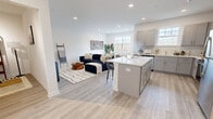 Located at 9 Hellers Lane in Jefferson, NJ, this thoughtfully designed single-floor residence offers a bright, open-concept living experience with contemporary finishes throughout. Light wood-tone flooring flows seamlessly across the entire space, tying each room together cohesively.

The kitchen is a standout feature, outfitted with gray shaker-style cabinetry, white quartz countertops, a subway tile backsplash, stainless steel appliances, and a central island with bar seating — ideal for both everyday cooking and entertaining. The kitchen opens directly into the dining area, which benefits from natural light through nearby windows, and the spacious living room beyond, creating a fluid, airy social space.

The bedroom is generously sized, featuring a large window with wooded views, light-filled walls, and access to a walk-in closet with built-in shelving. An additional den provides flexible space for a home office or secondary lounge area. Three closets throughout the unit offer ample storage.

The bathroom is clean and modern, featuring gray shaker-style cabinetry, a white quartz vanity top, a full tub-shower combination with tile surround, and light tile flooring. A private patio offers outdoor space with views of the surrounding natural landscape. Recessed lighting throughout keeps the entire residence bright and welcoming.