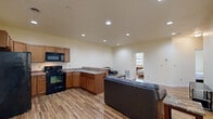 Located at 1026 Philadelphia St in Indiana, PA, this single-floor unit offers four bedrooms and two full bathrooms within a compact, efficiently arranged floor plan. The open-concept kitchen and living area forms the heart of the space, featuring warm hardwood-style flooring that extends throughout. Recessed ceiling lights illuminate the area evenly, creating a clean and functional atmosphere.

The kitchen is well-equipped with black appliances, including a refrigerator, electric range, and over-the-range microwave. Medium-toned wood cabinetry provides ample storage, while granite-patterned countertops offer practical workspace. A peninsula adds additional counter space and connects the kitchen to the living area, which comfortably accommodates seating and a media console.

The four bedrooms are modestly sized, with the primary bedroom being particularly compact. Each room features the same hardwood-style flooring and neutral wall tones. Select bedrooms receive natural light through windows with views of the surrounding neighborhood streetscape.

Both bathrooms include a full shower-tub combination and continue the consistent flooring found throughout the unit. A chrome towel rack and clean white fixtures contribute to a straightforward, functional design. The overall aesthetic is simple, modern, and well-maintained.
