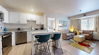 This single-floor, 2-bedroom, 1-bathroom unit at 411 W Maple St in Wichita, Kansas, is thoughtfully designed to maximize its compact footprint. Light wood-style flooring runs throughout, creating a cohesive and bright aesthetic across all rooms.

The open-concept kitchen and living area serves as the heart of the unit. The kitchen features white cabinetry, stainless steel appliances including a refrigerator, range, microwave, and dishwasher, and a central island with built-in shelving and seating for multiple bar stools. A stacked washer and dryer unit is conveniently integrated into the kitchen area, along with a closet for additional storage.

The living area accommodates comfortable seating and a wall-mounted television, with natural light provided by a window dressed with neutral curtains.

Both bedrooms feature light wood-style flooring, windows with natural light, wall-mounted or dresser-top televisions, and warm, neutral décor with contemporary artwork. The primary bedroom includes a full-length mirror and direct access to the bathroom.

The bathroom is finished with a white vanity, a tub-shower combination, and wood-style flooring, maintaining the clean, consistent palette found throughout the unit.