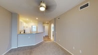 Located at 1100 Garden View in Encinitas, this single-floor residence presents a well-organized and functional layout designed for comfortable everyday living. The main living area features neutral-toned carpet flooring and warm beige walls, creating a clean and inviting atmosphere. A ceiling fan with a built-in light fixture is centrally mounted, providing both air circulation and ambient lighting throughout the space.

The kitchen flows seamlessly into the living area, anchored by a curved breakfast bar with a granite-style countertop that serves as a natural dividing element. White cabinetry and white appliances give the kitchen a bright, tidy appearance, while a window above the sink allows natural light to filter in. Recessed lighting in the kitchen ceiling adds additional illumination.

An elegant arched doorway leads from the main living area into a connecting hallway, adding a subtle architectural detail that softens the overall aesthetic. The hallway provides access to additional rooms within the unit. Hardwood-style flooring in the transition areas contrasts nicely with the carpeted living space. Neutral finishes and consistent design elements throughout give the space a cohesive, move-in-ready feel.