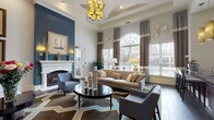 This single-story clubhouse is designed to impress, offering a sophisticated gathering space with a carefully curated interior that balances comfort and elegance. The main lounge area is defined by soaring ceilings and a coffered tray ceiling detail overhead, from which a striking multi-bulb chandelier with gold-toned accents is suspended. Large arched and double-hung windows flood the space with natural light, framed by layered brown and cream drapery panels that add texture and warmth.

A bold teal accent wall provides a dramatic backdrop for the white-mantled fireplace, which serves as a central focal point in the lounge. The surrounding seating arrangement includes a neutral linen sofa with decorative throw pillows, patterned accent chairs, and a dark round coffee table anchored by a geometric-patterned area rug in blue, gold, and gray tones. Wall sconces, framed artwork, and decorative plate arrangements contribute to the polished, gallery-like atmosphere throughout.

An adjacent kitchenette features dark espresso cabinetry, granite countertops, hardwood-style flooring, a mosaic tile backsplash, and recessed lighting—well-equipped to support community events and gatherings. The entry area showcases a marble-inlaid tile floor, adding a grand first impression to this thoughtfully appointed clubhouse.