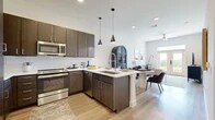 This well-appointed 2-bedroom, 2-bathroom residence is designed with a modern, open-concept layout that maximizes both functionality and comfort. The heart of the home is the kitchen, which features crisp white shaker cabinetry, a grey subway tile backsplash, stainless steel appliances including a refrigerator, dishwasher, and microwave, and a generously sized island with bar seating and pendant lighting overhead. Light hardwood-style flooring flows seamlessly from the kitchen into the living area, where floor-to-ceiling French doors and transom windows flood the space with natural light and open to a private balcony with scenic outdoor views. The living room offers a relaxed, airy ambiance enhanced by a ceiling fan and large windows. The primary bedroom is a comfortable retreat with soft carpet flooring, large windows framing outdoor views, and access to a dedicated closet. The second bedroom, equally well-lit, features its own window and closet space. Both bathrooms are finished with clean, neutral-toned tile flooring, white vanities with quartz-style countertops, and tub-shower combinations. Throughout the residence, a consistent palette of whites and warm neutrals creates a cohesive, modern aesthetic.
