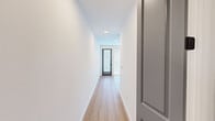 This thoughtfully designed one-bedroom, one-bathroom residence maximizes its compact footprint through an efficient, open-concept layout. A welcoming hallway with light hardwood flooring and crisp white walls leads into the main living area, where large floor-to-ceiling windows and a glass-paneled entry door flood the space with natural light and provide outdoor views.

The kitchen serves as a central hub, anchored by a substantial island with a white quartz countertop, an undermount stainless steel sink, and a matte black pull-down faucet. Stylish glass pendant lights with brass accents hang above the island, complementing the slate-gray cabinetry and stainless steel refrigerator. A sliding barn door adds a contemporary architectural touch, connecting the kitchen to adjacent spaces. Track lighting overhead provides additional illumination.

The bedroom offers a comfortable, carpeted retreat with a ceiling fan and light fixture. Direct access to the bathroom creates a convenient en-suite feel. The bathroom is finished with large-format tile surrounding a soaking tub and shower combo, accented by dark bronze fixtures and hardware, paired with dark wood cabinetry and a well-lit vanity mirror. A dedicated closet provides practical storage. Throughout the residence, clean lines, neutral tones, and modern hardware create a cohesive, contemporary aesthetic.