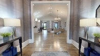 The Stone Park Boulevard Clubhouse in Pike Road, Alabama, is a thoughtfully designed single-story community facility that blends upscale aesthetics with practical amenities. The grand entrance features a striking arched wood door framed by sidelights, opening into a foyer adorned with textured gray wallcovering, a crystal chandelier, and rich hardwood flooring that flows throughout the entire space.

The main gathering area is anchored by soaring vaulted ceilings, recessed lighting, and an elegant chandelier, creating an airy, welcoming atmosphere. A stylish lounge area with neutral-toned seating, a bold sculptural pendant light, and navy accent pillows provides a comfortable setting for socializing. Adjacent to the lounge, the fully appointed kitchen features white shaker cabinetry, quartz countertops, a center island with bar seating, pendant lighting, and wall-mounted televisions — ideal for community events.

A dedicated conference and business area includes a spacious meeting room and a private workspace, both finished with patterned carpet and contemporary furnishings. The entertainment wing offers a relaxed lounge with a large-format Scrabble board and mounted TV, as well as a game room complete with a pool table and shuffleboard. Large windows throughout invite abundant natural light, enhancing the clubhouse's refined yet approachable character.