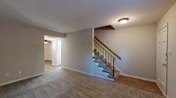 Located at 263 Clemwood Pkwy in Hampton, Virginia, this two-story home offers a practical and well-organized layout spread evenly across two floors. The main level features a living room with neutral carpet, a ceiling-mounted light fixture, and a staircase with a wood-and-iron railing that leads to the upper level. The kitchen is equipped with warm oak cabinetry, dark countertops, a black appliance suite including an electric range and dishwasher, and wood-look flooring. A door in the kitchen provides convenient exterior access, and windows allow for natural light throughout. The main floor is completed by hallway access, a bathroom, and a utility room. Upstairs, two carpeted bedrooms offer comfortable retreats. The primary bedroom is a generously sized room with a ceiling fan and light kit. The second bedroom features louvered closet doors, a natural light window, and dark carpet. Both bathrooms are finished with white vanities, clean countertops, and simple, functional fixtures. Throughout the home, neutral wall tones, carpet in living and bedroom areas, and wood-look flooring in the kitchen create a cohesive and move-in ready aesthetic.