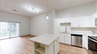Located at 24560 E Applewood Cir in Aurora, CO, this one-bedroom, one-bathroom unit offers a thoughtfully designed layout across a single floor. The open-concept kitchen and living area is a standout feature, showcasing crisp white shaker cabinetry with gold hardware, quartz countertops, and a full suite of stainless steel appliances including a range, over-the-range microwave, dishwasher, and refrigerator. A central kitchen island with built-in shelving and a pendant light above adds both function and style. Track lighting illuminates the space, which flows seamlessly into the living area via warm-toned hardwood-style flooring. A sliding glass door brings in natural light and provides outdoor access. The bedroom is carpeted for comfort and features tall ceilings, a window with views of surrounding greenery, and direct access to a generously sized walk-in closet outfitted with wire shelving and built-in storage units. The bathroom includes a tiled shower/tub combination, wood-toned cabinetry with overhead storage, and hardwood-style flooring. Clean white walls and consistent finishes throughout lend the space a bright, modern, and cohesive aesthetic.