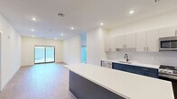 Located at 555 Northfield Avenue in West Orange, NJ, this thoughtfully designed one-bedroom, one-bathroom unit offers a clean, contemporary aesthetic across a single floor. The open-concept kitchen and living area serves as the heart of the home, featuring light wood-tone flooring, recessed lighting, and sliding glass doors that lead directly to a private patio. The kitchen is well-appointed with two-tone cabinetry — crisp white upper cabinets paired with bold navy lower cabinets — a white quartz countertop, stainless steel appliances including a gas range, microwave, dishwasher, and refrigerator, and a center island for additional prep and seating space. A textured tile backsplash adds a refined finishing touch. The spacious primary bedroom features a large window with outdoor views and generous closet space, supported by three closets throughout the unit. The bathroom is finished with large-format marble-look tile flooring, a dark vanity with gold hardware, a round mirror, and matte black accessories. Additional highlights include a versatile den, dedicated in-unit laundry, and a consistent use of neutral tones that create a bright, modern ambiance throughout.