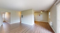 This single-floor unit is designed with a clean, functional layout that makes efficient use of its space. The open living area is finished with wood-look vinyl flooring and neutral-toned walls, creating a bright and versatile environment. A ceiling fan with a light fixture provides both comfort and overhead illumination, while a wall-mounted electrical panel is neatly integrated into the space. A sliding glass door in the living area floods the room with natural light and provides direct views of the surrounding greenery.

The kitchen is well-appointed, featuring rich dark cabinetry with modern hardware, white quartz-style countertops, and a marble-style tile backsplash. Stainless steel appliances, including a range, over-the-range microwave, dishwasher, and refrigerator, complete the space, which also includes wood-look flooring for easy maintenance.

The bedrooms are carpeted for comfort and include closet storage. Natural light enters through windows fitted with blinds. The bathroom offers a dark wood vanity with a white countertop, tile flooring, a baseboard heater, and a window for ventilation. A narrow entryway with a glass-paneled door and baseboard heating provides a welcoming transition into the unit.