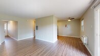 This single-floor unit is designed with a clean, functional layout that makes efficient use of its space. The open living area is finished with wood-look vinyl flooring and neutral-toned walls, creating a bright and versatile environment. A ceiling fan with a light fixture provides both comfort and overhead illumination, while a wall-mounted electrical panel is neatly integrated into the space. A sliding glass door in the living area floods the room with natural light and provides direct views of the surrounding greenery.

The kitchen is well-appointed, featuring rich dark cabinetry with modern hardware, white quartz-style countertops, and a marble-style tile backsplash. Stainless steel appliances, including a range, over-the-range microwave, dishwasher, and refrigerator, complete the space, which also includes wood-look flooring for easy maintenance.

The bedrooms are carpeted for comfort and include closet storage. Natural light enters through windows fitted with blinds. The bathroom offers a dark wood vanity with a white countertop, tile flooring, a baseboard heater, and a window for ventilation. A narrow entryway with a glass-paneled door and baseboard heating provides a welcoming transition into the unit.
