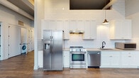 Located at 122 Parsons Ave in Columbus, Ohio, this single-floor unit blends modern design with industrial character. The open-concept living area features rich hardwood-style flooring, soaring ceilings with exposed ductwork, and pendant lighting that adds a loft-inspired aesthetic. Large windows flood the space with natural light, offering views of the surrounding neighborhood.

The kitchen is a standout feature, showcasing white shaker cabinetry, full subway tile backsplash extending to the ceiling, and a complete suite of stainless steel appliances including a side-by-side refrigerator, range, dishwasher, and microwave. The generous counter space and ample cabinetry make it both functional and visually striking.

The unit includes two bathrooms: one with a sleek walk-in tile shower, a white vanity with matte black fixtures, and a bold dark-framed mirror; the other featuring a full soaking tub and tiled floors. A dedicated walk-in closet with built-in wire shelving and carpeted flooring provides excellent storage.

Hallways with exposed structural elements connect the rooms seamlessly, reinforcing the industrial-modern character throughout. The thoughtful layout and high-quality finishes make this Columbus unit a compelling and well-appointed space.