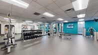This fitness center offers a generously sized, single-floor workout facility designed to accommodate a full range of exercise needs. The space is divided into distinct functional zones, providing an organized and efficient layout for both strength training and cardiovascular activity.

The strength training area is prominently featured, equipped with multi-station cable machines, adjustable benches, and a fully stocked dumbbell rack spanning a wide range of weights. Floor-to-ceiling mirrors line the walls, visually expanding the space and allowing users to monitor their form. A vibrant teal accent wall, paired with a wall-mounted flat-screen television, adds energy and visual interest to this zone.

The cardio area features treadmills and an elliptical trainer, set against a whitewashed brick-style wall adorned with a bold motivational mural reading "Be Bold. Be Brave. Be You." A rack of medicine balls and stability balls rounds out the functional fitness offerings in this section.

Throughout the facility, durable rubber flooring provides safety and comfort underfoot, while a suspended drop-tile ceiling with recessed fluorescent lighting ensures consistent, bright illumination. Natural light filters in through windows along one wall. The Harbor Fit branding is visible throughout, contributing to a cohesive and professional atmosphere suited for a wide range of fitness pursuits.