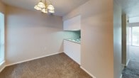This single-floor unit is designed with a neutral, functional aesthetic throughout. The living room is a generously sized, carpet-floored space anchored by a large sliding glass door fitted with vertical blinds, allowing ample natural light and providing views of surrounding greenery. The dining area sits adjacent to the kitchen, illuminated by a classic brass chandelier, and connects to the kitchen via a convenient pass-through opening. The kitchen features coil-burner electric cooktop set into a laminate countertop, cabinetry with dark countertops, and a built-in range hood above, all within a compact, efficient layout.

The bedrooms are carpeted and well-sized, with neutral-toned walls and windows dressed with horizontal blinds for natural light control. One bedroom is notably well-equipped with two side-by-side bifold closets, offering generous storage capacity. Both bathrooms maintain a consistent design, featuring white cabinetry, louvered mirror cabinets, dark laminate countertops with white sinks, and tile flooring. One bathroom includes a shower-tub combination. Throughout the unit, white trim and soft beige tones create a clean, cohesive atmosphere.