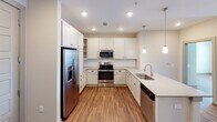 This single-floor residence offers a thoughtfully designed layout that balances open communal areas with well-defined private spaces. Rich wood-look flooring runs seamlessly throughout, lending warmth and visual continuity to every room.

The kitchen serves as a functional centerpiece, featuring white shaker-style cabinetry, quartz countertops, stainless steel appliances including a French door refrigerator with ice maker, electric range, microwave, and dishwasher. A peninsula with an undermount sink and pendant lighting above creates a natural transition into the open living and dining areas, which benefit from natural light through large windows and a glass-panel entry door fitted with blinds.

The bedrooms are generously proportioned, each equipped with ceiling fans and ample closet space. The primary suite connects directly to a walk-in closet outfitted with multi-tier wire shelving systems and leads to an en-suite bathroom with a walk-in glass shower, quartz vanity, and undermount sink. A second full bathroom offers a tub-shower combination, matching quartz vanity, and access to an additional walk-in closet. A separate, expansive walk-in closet provides further storage capacity. The space also features a barn-style sliding door accent and recessed lighting throughout, completing a clean, contemporary interior.