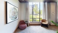 Located at 412 Summer St in Abington, Massachusetts, this single-floor space offers a well-appointed layout across a compact but efficiently utilized footprint. The hallway entry features glass-paneled doors that invite natural light in while providing a clear sightline to a warm reception area finished in rich wood tones and large-format tile flooring, setting a polished and professional tone from the moment of arrival.

The living room is a standout area, anchored by a large floor-to-ceiling window that frames sweeping views of a lush green lawn and surrounding buildings. Neutral-toned carpet, elegant draping curtains, and contemporary seating create a comfortable and inviting atmosphere bathed in natural light.

Among the additional rooms, a private nook or workspace features dramatic stone-look wall panels with flowing, marble-like veining in soft creams and warm taupes, complemented by a clean white built-in desk surface and upholstered seating — ideal for focused work or quiet reflection.

Two bathrooms round out the layout, contributing to the space's practical functionality. Throughout, the design blends modern finishes — including warm wood accents, plush carpeting, and refined stonework — to create a cohesive, sophisticated ambiance suited for both comfort and purposeful use.