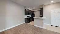 This single-story 1-bedroom, 1-bathroom Harbor unit offers a well-organized layout designed for comfortable everyday living. The living area is carpeted and bathed in natural light from a sliding glass door that opens to a private balcony, providing views of the surrounding neighborhood. A tiled entryway transitions smoothly into the living space, creating a practical and welcoming introduction to the unit.

The kitchen is a standout feature, equipped with rich dark espresso cabinetry that extends floor to ceiling, offering generous storage throughout. White countertops provide a clean contrast, while black appliances—including a range, refrigerator, and built-in microwave—complete the functional setup. A peninsula with a sink and bar-style overhang connects the kitchen to the living area, ideal for casual dining or entertaining.

The bedroom is spacious and carpeted, featuring tray ceiling detailing that adds architectural interest. A large walk-in closet provides ample storage. Natural light filters in through well-placed windows offering views of neighboring architecture. The bathroom features a dual-sink vanity with dark cabinetry, white countertops, tile flooring, and a large mirror, delivering a clean, cohesive aesthetic throughout.