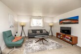 This thoughtfully laid-out 2-bedroom, 2-bathroom single-floor home in Williamsburg, Iowa, offers a comfortable and functional living experience. The living room serves as the heart of the home, featuring plush carpeting, a textured ceiling, and a window that allows natural light to fill the space. The room comfortably accommodates a seating area centered around a glass coffee table, with ample wall space for decor. Adjacent to the living area, the combined dining room and kitchen provide a seamless flow for everyday living. The kitchen features warm wood cabinetry, white appliances including an electric range, a double stainless steel sink, and durable hardwood-style flooring. The dining area connects directly, offering space for a round glass dining table and additional storage. The primary bedroom includes soft carpeting, a closet, and a window that brings in natural light. The second bedroom, similarly carpeted, also features a window and closet access. Both bathrooms are well-appointed — one includes a wood-toned vanity with medicine cabinet mirror, while the other features a full tub-shower combo with tiled surround. A hallway connects all rooms, creating an efficient and cohesive floor plan throughout.