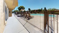 Located at 532 Broadway in El Cajon, California, this single-story community amenity space is designed to support comfortable, everyday living for its residents. The exterior features a classic stucco finish in warm beige tones, consistent with the surrounding multi-story residential buildings that frame the property.

At the heart of the outdoor area is a sparkling swimming pool, enclosed by a sturdy iron fence and surrounded by a spacious concrete pool deck. The poolside area is furnished with lounge chairs and shaded by a large patio umbrella, creating a welcoming space for relaxation under the Southern California sun. Mature trees and landscaping line the perimeter, offering a touch of greenery against the open sky.

Adjacent to the pool area, a wide concrete walkway runs alongside the building, providing convenient pedestrian access throughout the grounds. The pathway connects key amenity areas and benefits from abundant natural light throughout the day.

A dedicated on-site laundry facility is also available to residents, clearly marked with posted operating hours of 8am to 10pm. The facility entrance features a windowed door with blinds, set within the same textured stucco exterior. Together, these amenities create a functional and community-oriented outdoor environment suited to the Southern California lifestyle.
