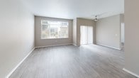 This single-floor residence offers a thoughtfully designed layout that balances open living spaces with functional private areas. The living room serves as the heart of the unit, featuring light wood-look flooring, neutral gray walls, and an abundance of natural light streaming through a large picture window and sliding glass door. A ceiling fan adds practical comfort, while the outdoor views provide a pleasant backdrop.

The semi-open kitchen is efficiently arranged in a galley style, featuring dark countertops that contrast cleanly with white lower cabinetry accented by light wood upper cabinets. Stainless steel appliances, including a full-size refrigerator and dishwasher, are complemented by a stainless sink. Track lighting overhead ensures ample illumination. A half-wall pass-through connects the kitchen to the living area, maintaining an open feel while defining the separate spaces.

The bathroom includes a wood-toned vanity with a dark countertop, an overhead vanity mirror, a combination tub and shower, and light wood-look flooring. A dedicated walk-in closet finished with plush carpet and wire shelving systems provides generous storage capacity. Throughout the residence, consistent use of light tones and hardwood-style flooring creates a cohesive, modern ambiance.