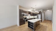 Located in Dallas's vibrant McKinney Avenue corridor, this well-appointed 2-bedroom, 1-bathroom residence offers a thoughtfully designed single-floor layout. The open-concept kitchen and living area serves as the heart of the home, showcasing rich dark-espresso cabinetry, a full suite of stainless steel appliances including a refrigerator, electric range, microwave, and dishwasher, and crisp white countertops. A central kitchen island with built-in shelving provides additional storage and prep space, while a modern chandelier adds a refined touch overhead. Warm hardwood-style flooring flows throughout the main living areas, complemented by recessed lighting and built-in wall shelving. A bright hallway with a sliding barn door connects the living space to the private quarters. The primary bedroom features sliding glass doors opening to a private balcony with outdoor views, while the second bedroom offers plush carpeting, a ceiling fan, and a large window with natural light. The full bathroom includes a soaking tub, a separate glass-enclosed shower, tile flooring, and dark wood vanity cabinetry. Additional highlights include a spacious walk-in closet with built-in shelving and hanging rods, a dedicated laundry area, and a secondary reach-in closet with hardwood-style flooring.